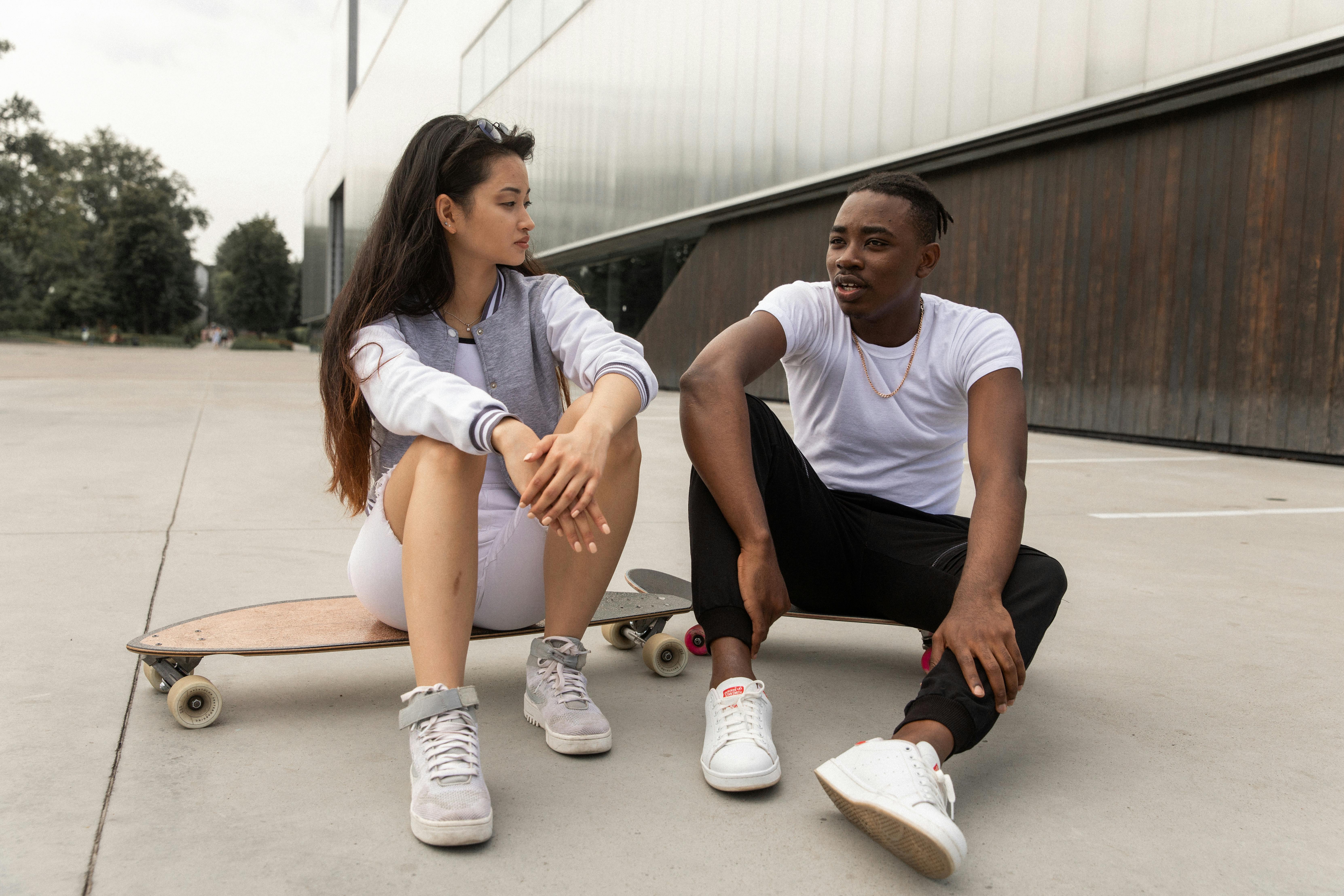 Woman sitting on a skateboard while her male partner is sitting on the floor, communicating.