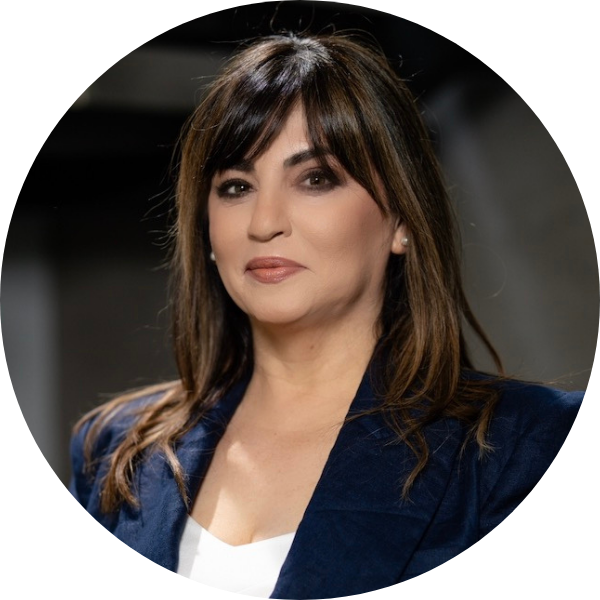 A woman with medium-length brown hair wearing a navy blazer and white top poses in front of a blurred background.